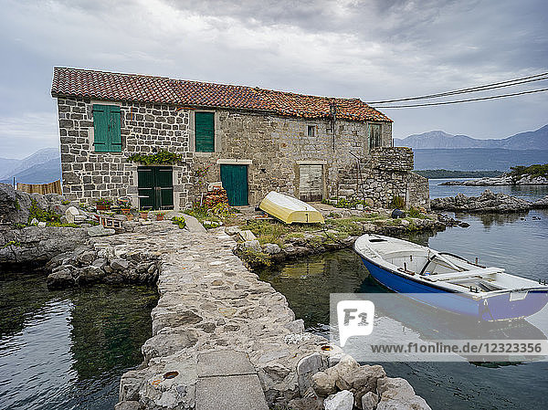 Ein kleines Boot legt vor einem Steinhaus in der Bucht von Kotor an; Bjelila  Opstina Tivat  Montenegro