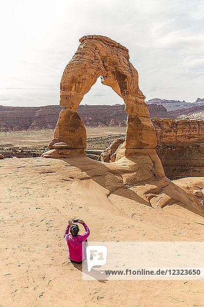 Frau nimmt ein Handy-Foto von Delicate Arch  Arches National Park; Moab  Utah  Vereinigte Staaten von Amerika