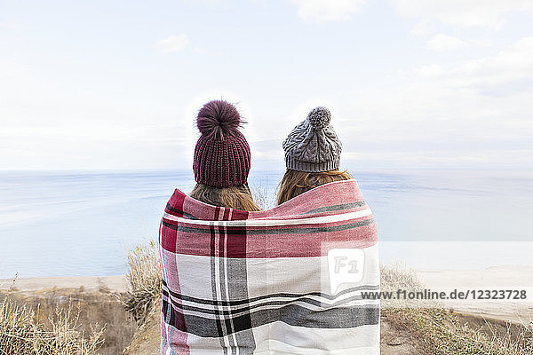 Two friends wrapped in a blanket standing on bluffs looking out over Lake Ontario; Scarborough  Ontario  Canada