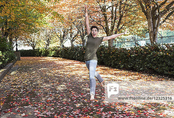 Eine junge Frau tanzt auf einem Weg in einem Park im Herbst; New Westminster  British Columbia  Kanada