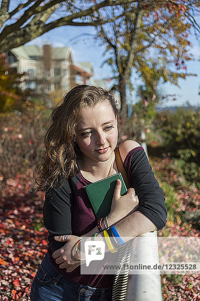 Eine junge Frau sitzt auf einer Parkbank und drückt ein Buch an ihre Brust; New Westminster  British Columbia  Kanada