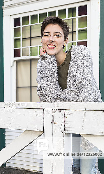 Porträt einer jungen Frau mit kurzen brünetten Haaren  die sich lächelnd an ein Geländer lehnt