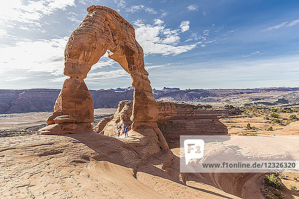 Eine Wanderin steht feiernd unter dem Delicate Arch im Arches National Park; Moab  Utah  Vereinigte Staaten von Amerika