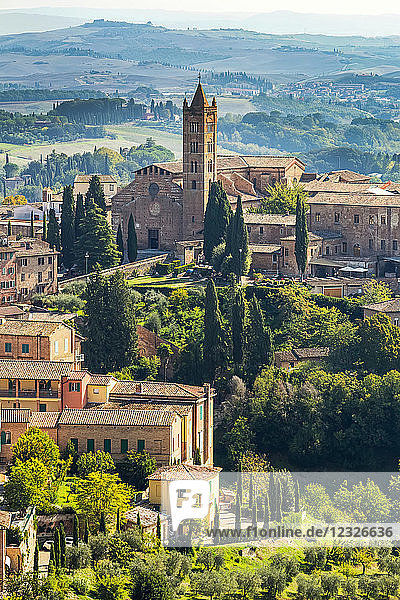 Steingebäude und Kirche in einer Landschaft mit Bäumen und sanften Hügeln im Hintergrund; Siena  Toskana  Italien