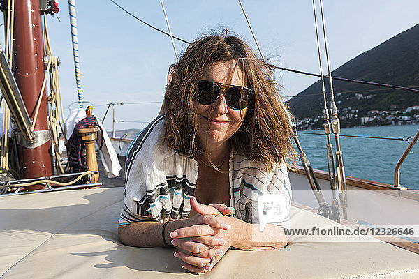 Eine Frau liegt mit zerzaustem Haar auf dem Deck eines Segelbootes und schaut in die Kamera an der Küste von Montenegro; Montenegro