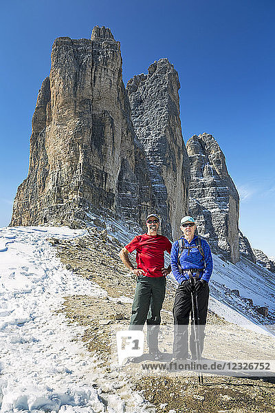 Male and female hikers standing on rocky slope with dramatic mountain spires and blue sky; Sesto  Bolzano  Italy