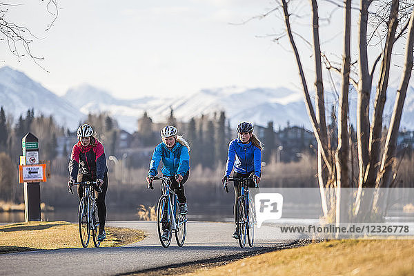 Three young women riding their bicycles on a trail along the water's edge; Anchorage  Alaska  United States of America