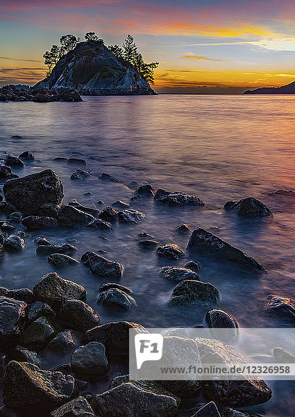 Goldenes Sonnenlicht beleuchtet die Wolken in der Ferne und nasse Felsen entlang der Küste; Vancouver  British Columbia  Kanada