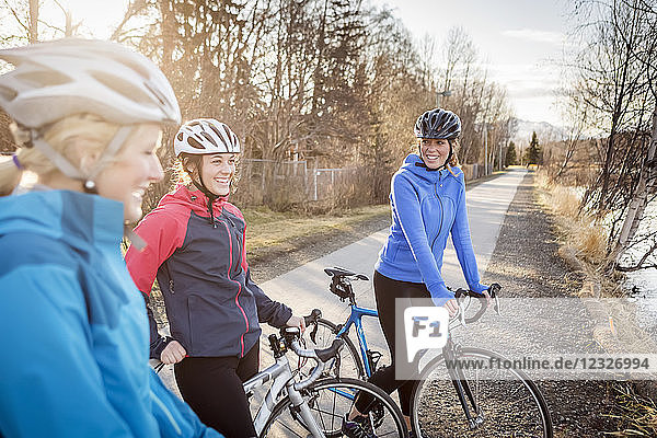 Drei junge Frauen auf ihren Fahrrädern auf einem Weg bei Sonnenaufgang; Anchorage  Alaska  Vereinigte Staaten von Amerika