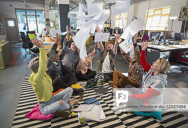 Playful  enthusiastic creative business team throwing paperwork overhead in open plan office