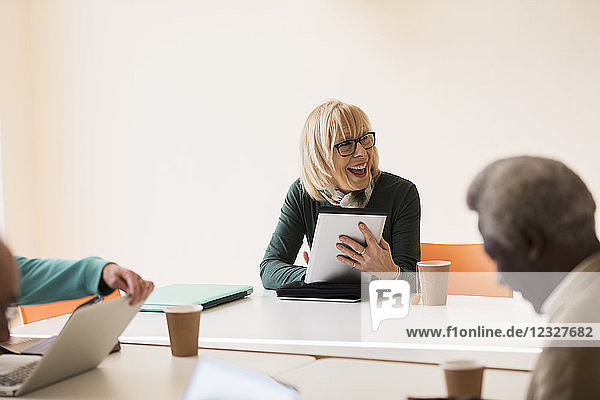 Smiling  confident senior businesswoman with digital tablet leading conference room meeting