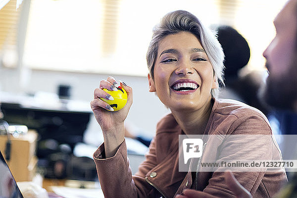 Laughing creative businesswoman squeezing stress ball in office