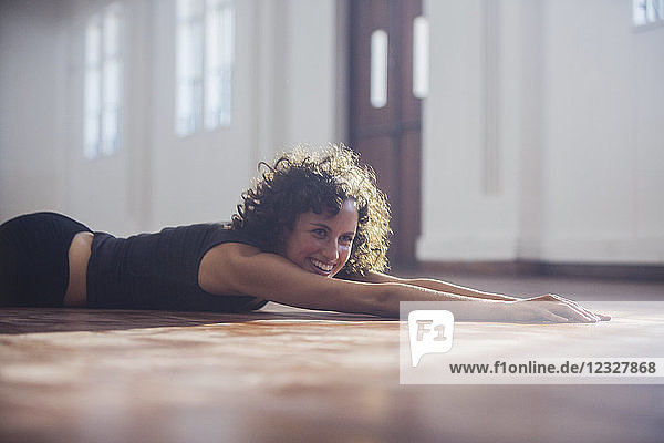 Smiling carefree young female dancer stretching on dance studio floor