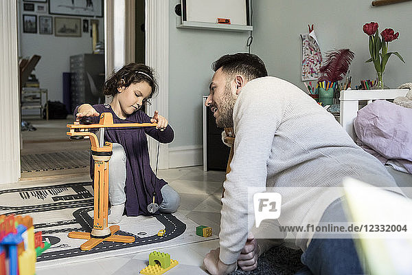 Father looking at daughter playing with crane toy in living room at home