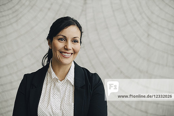 Smiling businesswoman standing against wall at office