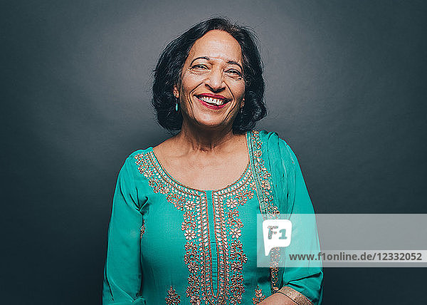 Portrait of smiling senior woman wearing salwar kameez against gray background