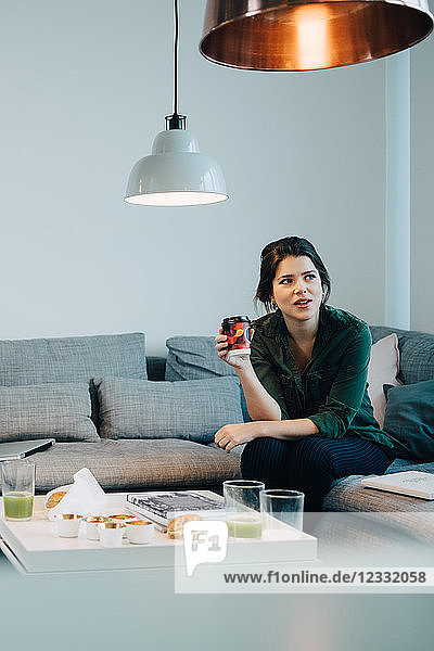 Mid adult businesswoman sitting with coffee on sofa at creative office