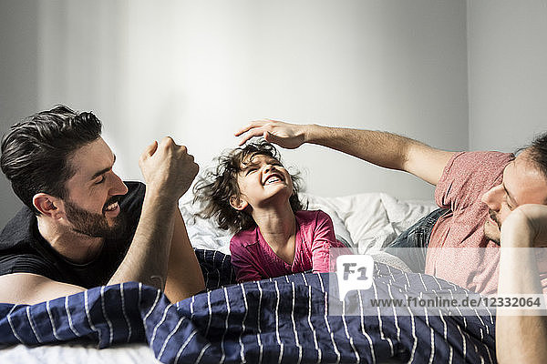Fathers playing with cheerful daughter while lying on bed at home