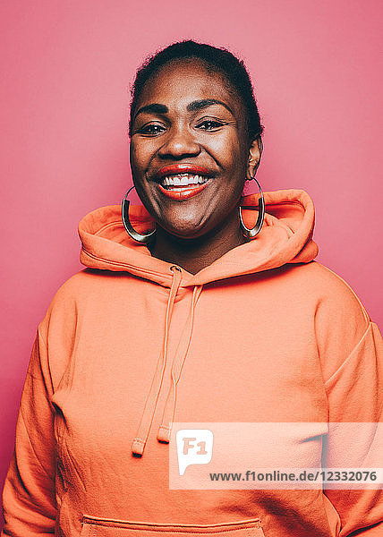 Portrait of smiling mid adult woman wearing orange hooded jacket over pink background
