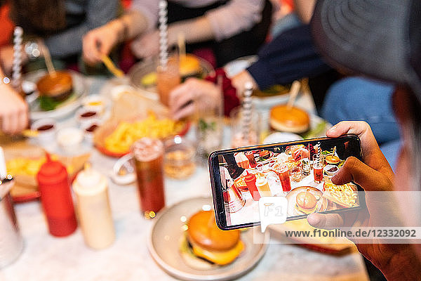 Cropped image of teenage boy photographing food and drinks served on table at restaurant