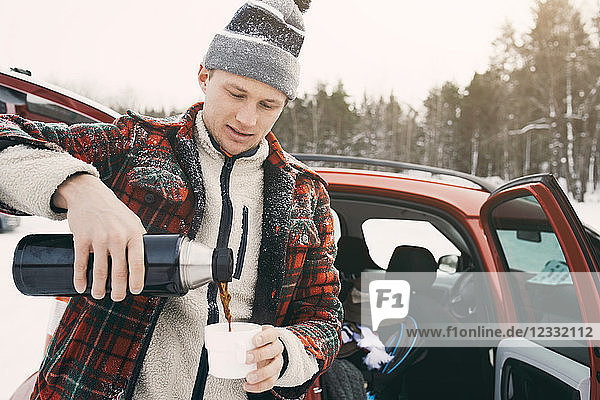 Mid adult man pouring coffee from insulated drink container while standing by car