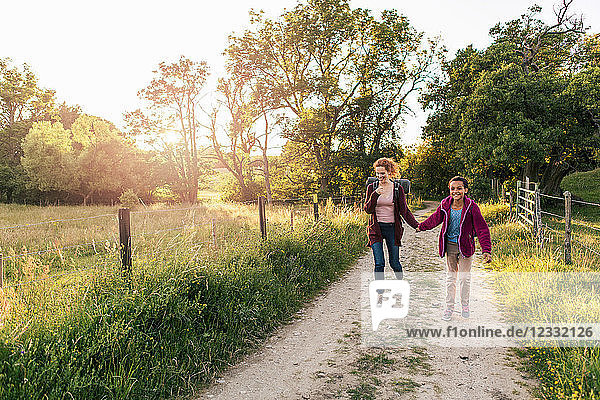 Full length of smiling mother and daughter holding hands walking on dirt road in forest