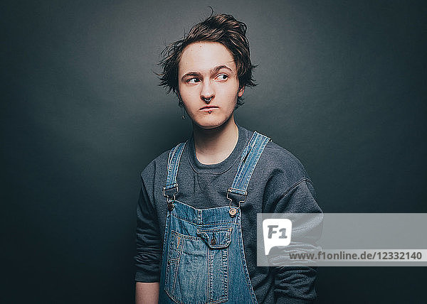 Young man wearing overalls while looking sideways over gray background