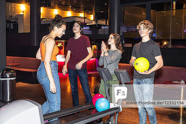 Happy teenage friends standing by rack at bowling alley