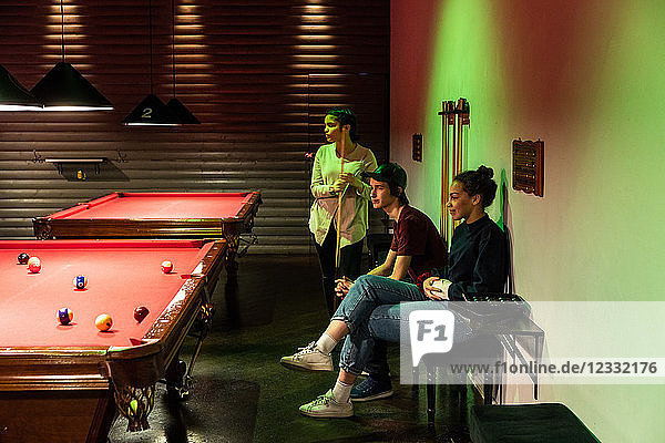 Multi-ethnic friends looking at cue balls on illuminated red pool table