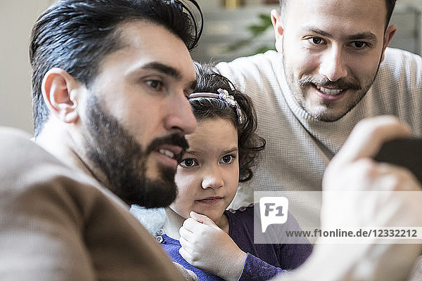 Fathers with curious daughter looking at smart phone while sitting at home