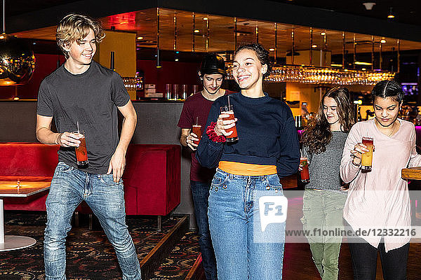 Smiling multi-ethnic teenage friends holding drinks while walking at restaurant