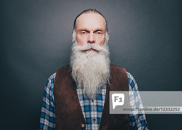 Portrait of confident senior man with long white beard against gray background