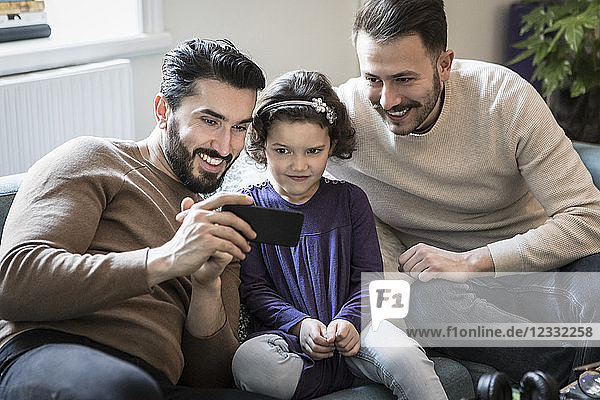 Fathers and daughter looking at smart phone while sitting on sofa at home