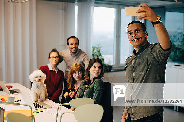 Smiling businessman taking selfie with colleagues at dog at creative office