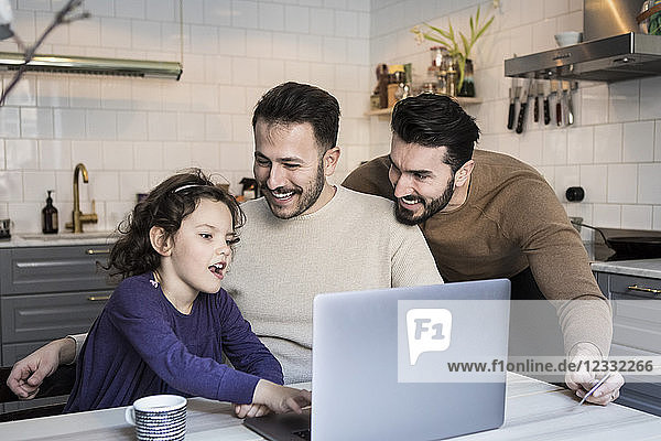 Happy fathers looking at daughter using laptop at table in kitchen