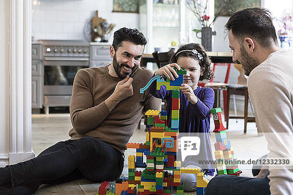 Gay parents looking at daughter playing with blocks at home