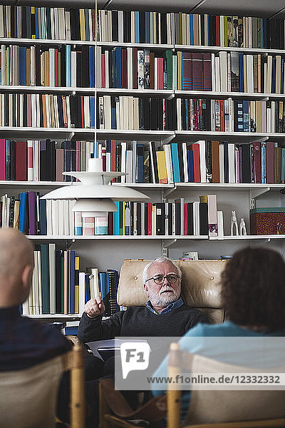 Senior therapist explaining couple while sitting against bookshelf