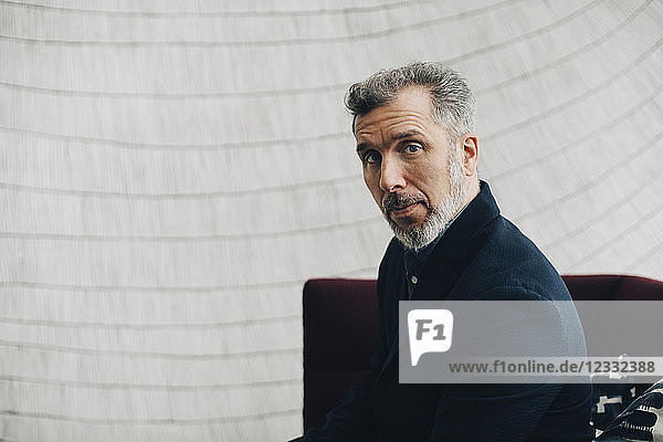 Portrait of mature businessman sitting on couch against wall at office