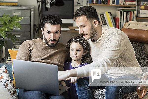 Fathers showing laptop to daughter while sitting on chairs at home