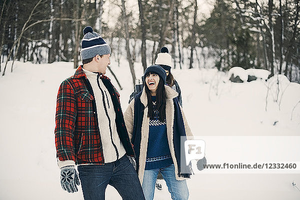Happy friends talking while walking on snow covered field