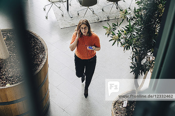 High angle view of businesswoman using mobile phone while walking in office