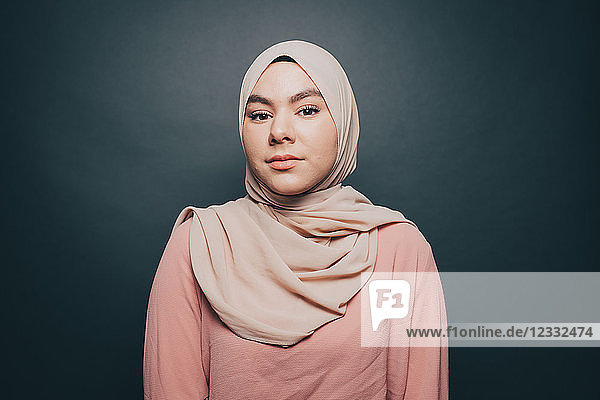 Portrait of confident young woman wearing hijab against gray background