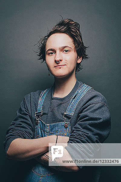 Portrait of trendy young man standing arms crossed over gray background