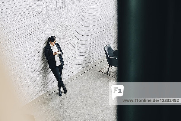High angle view of woman using mobile phone while leaning on wall at office