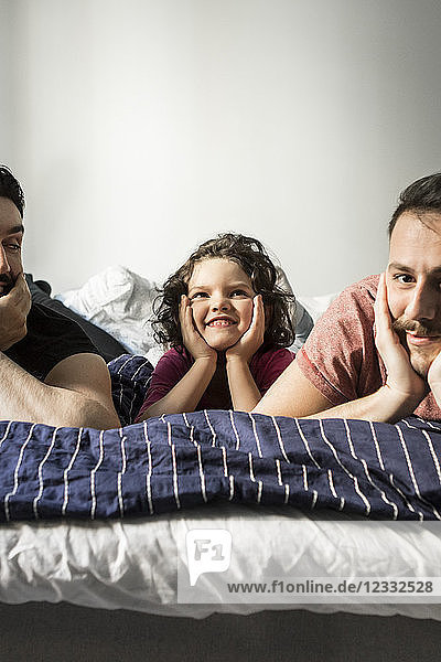 Fathers and daughter lying with head in hands on bed against wall
