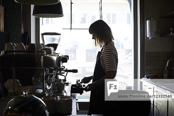 Side view of female barista preparing coffee by window at cafe