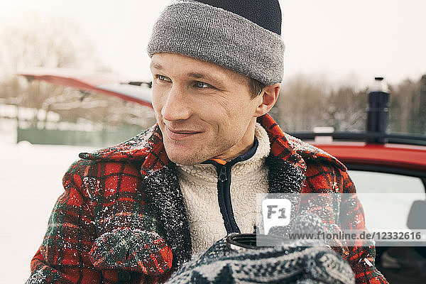 Close-up of thoughtful smiling man having coffee against car