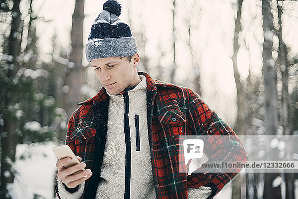 Man using smart phone while standing at park during winter