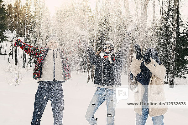 Playful friends throwing snow while standing on field at park