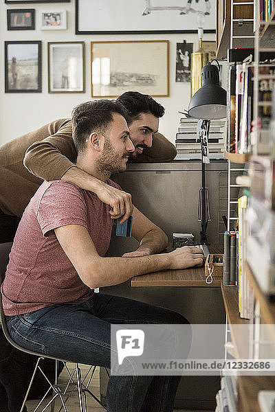 Side view of gay couple shopping online through computer at home